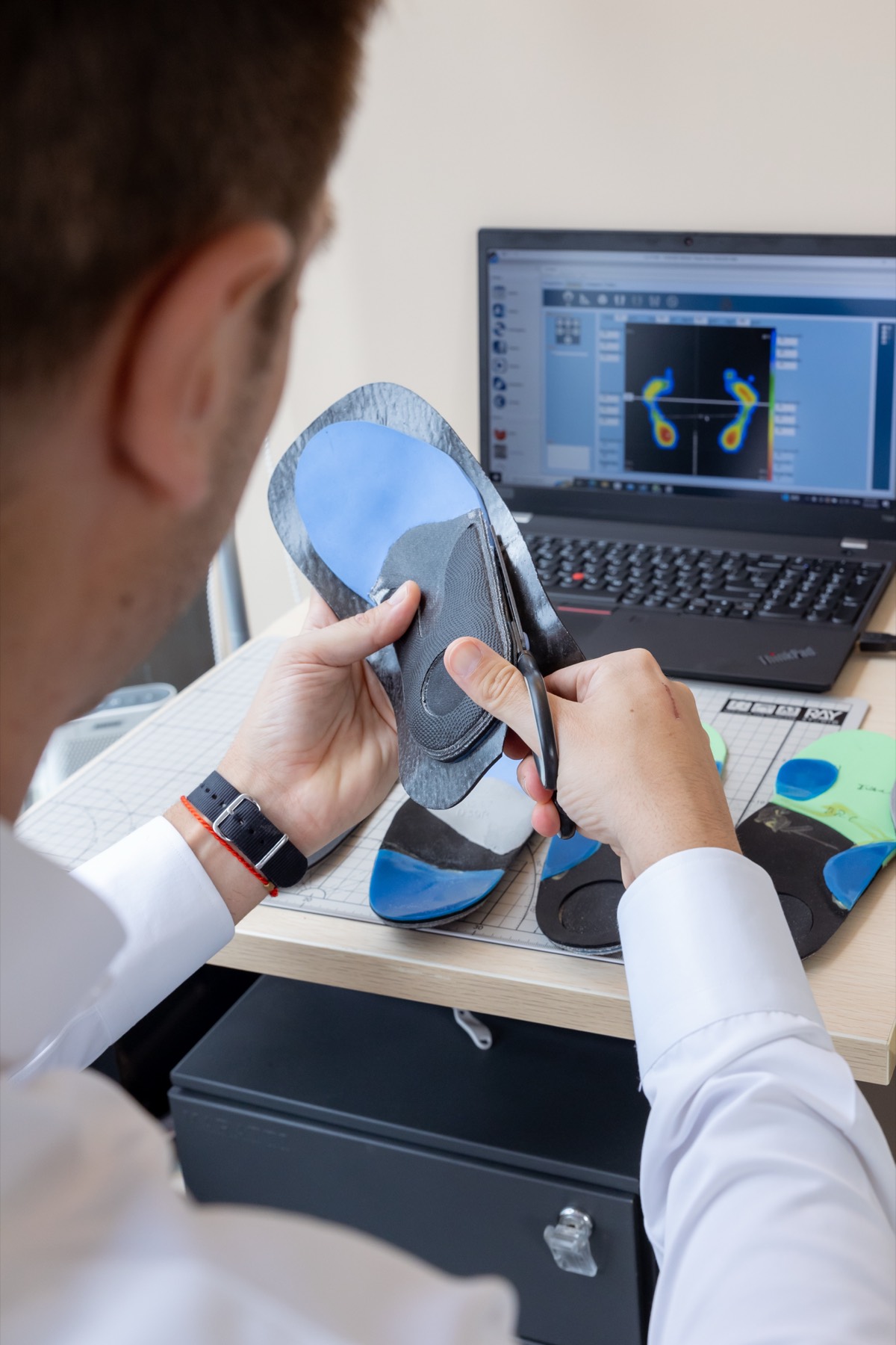 Albin Brion trimming a finished custom-made carbon-fibre orthotic at his bench, the 3D pressure reading on screen behind